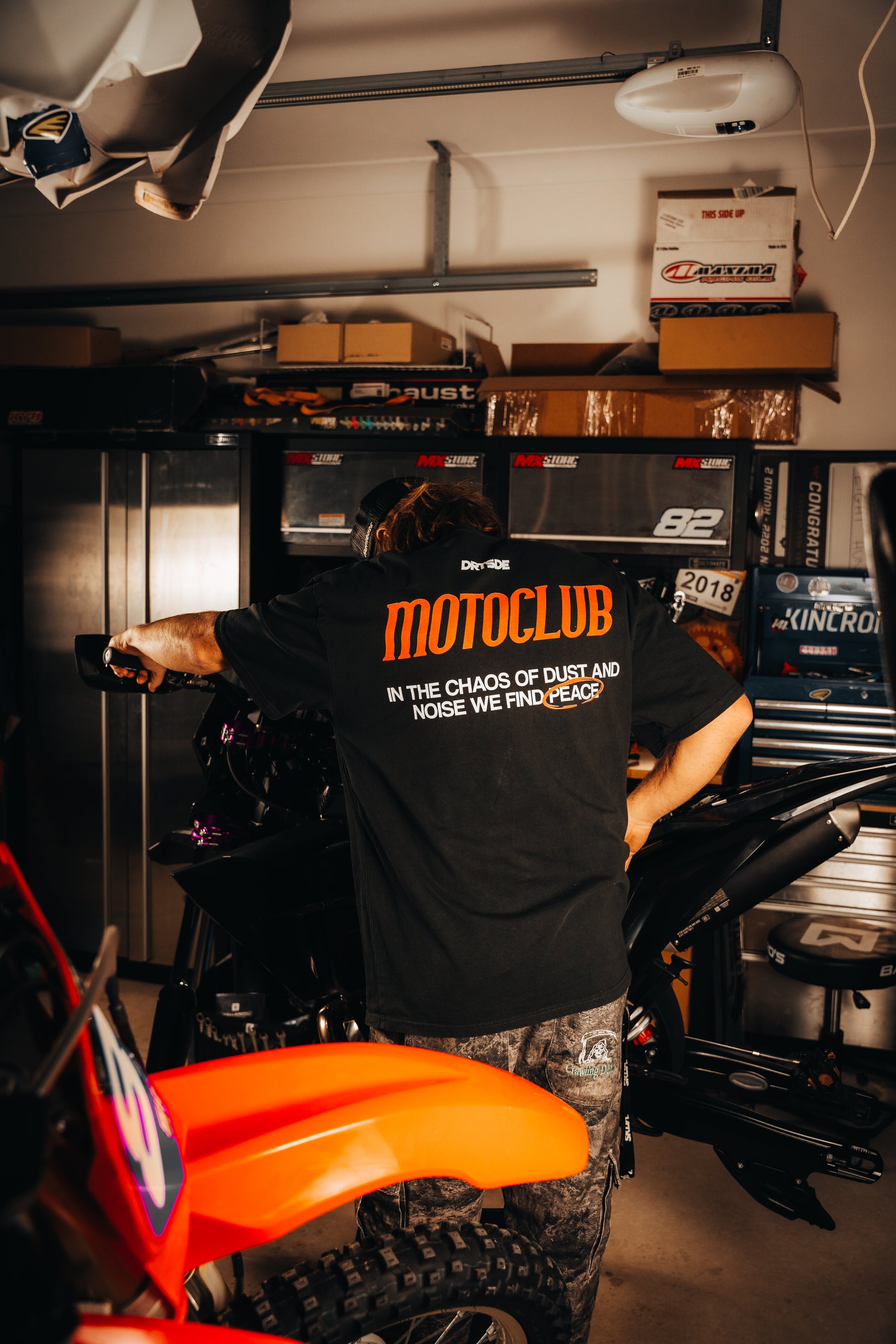 Person wearing a black t-shirt with 'Motoclub' text in a garage setting.