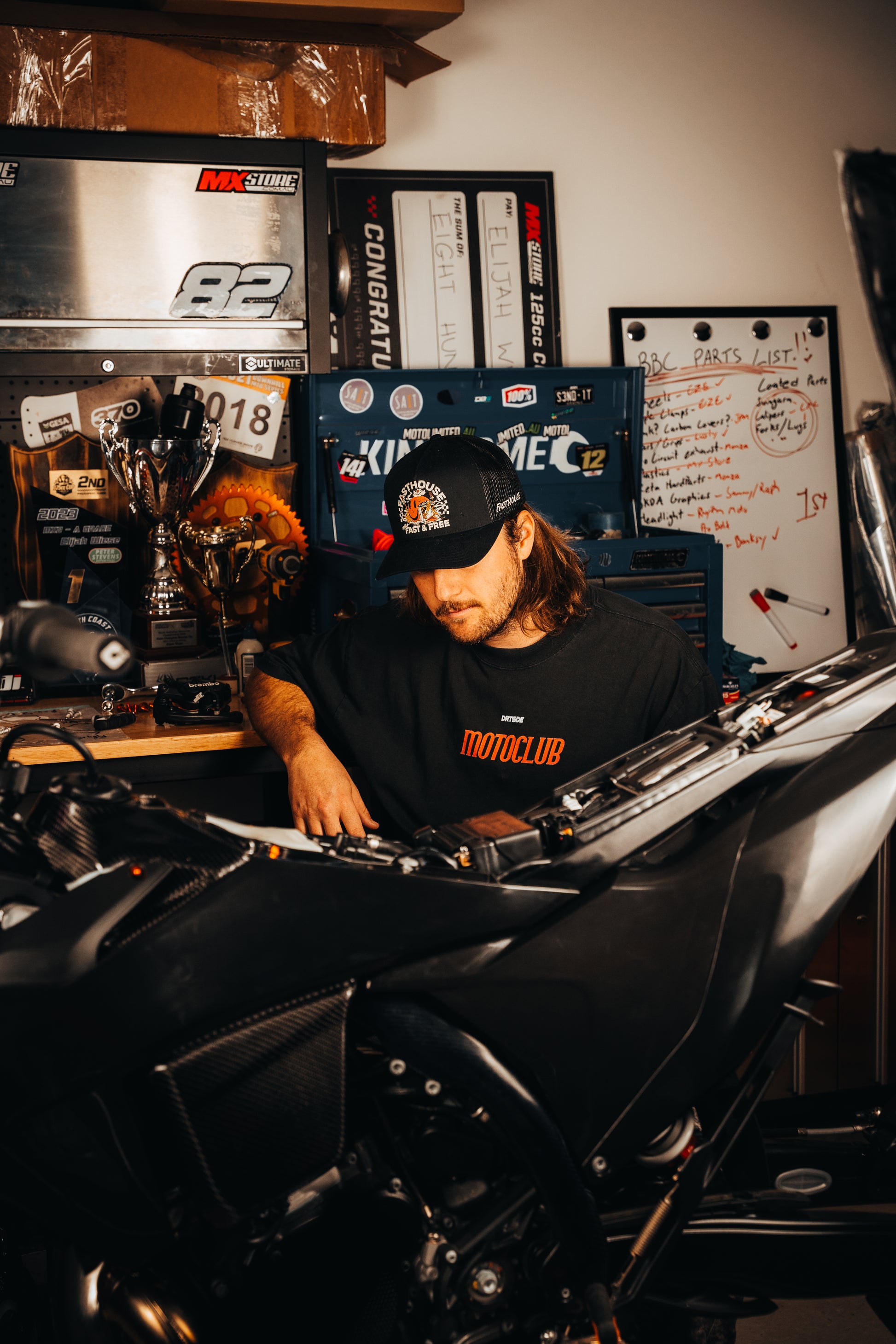 Person working on a motorcycle in a garage with various automotive memorabilia in the background.